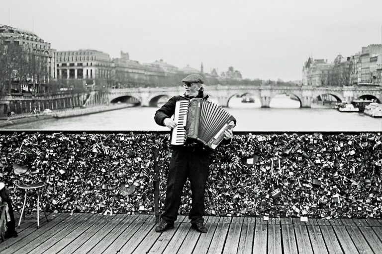Street musician playing accordion on the Pont des Arts bridge in Paris.