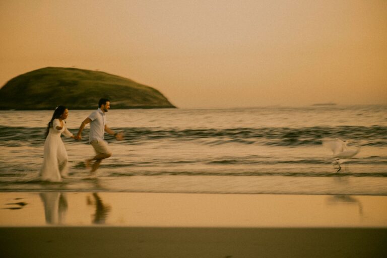 A couple runs joyfully on a beach at sunset with a scenic view of Rio de Janeiro.