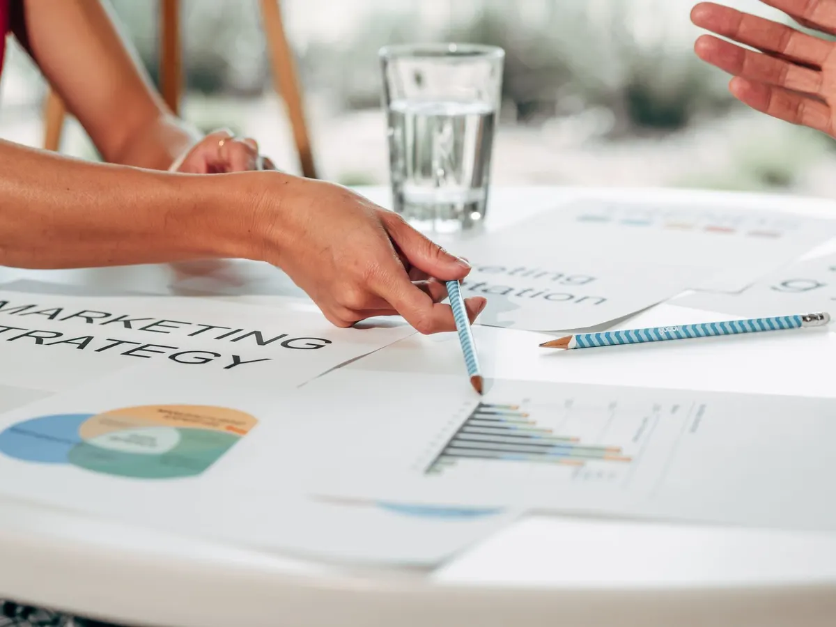 Hands discussing marketing strategy with charts in an office setting.