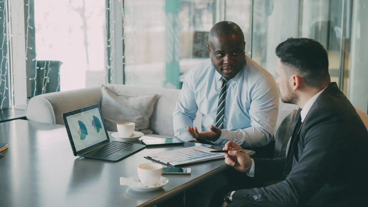 Two business professionals engaged in discussion over laptops and documents.