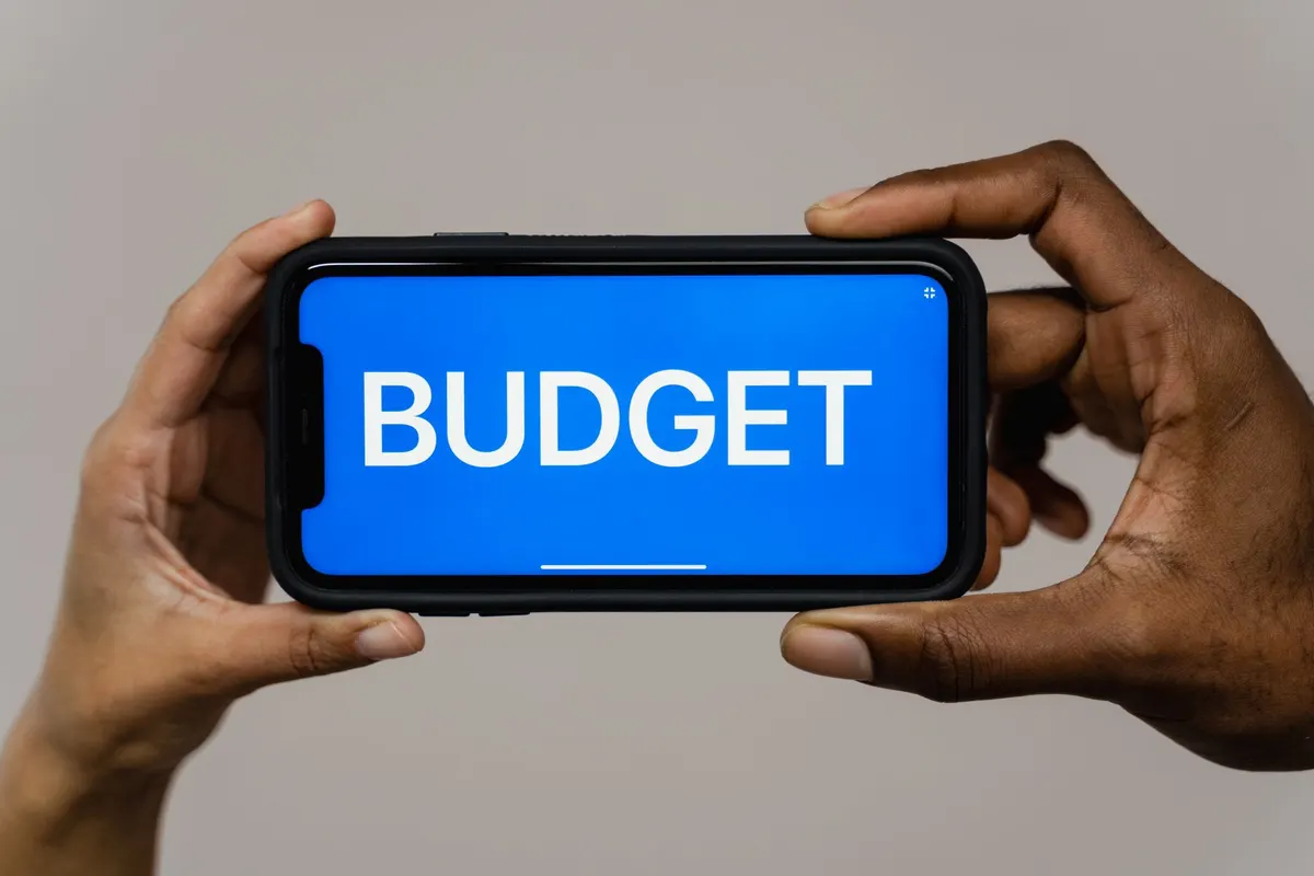 Two hands hold a smartphone displaying the word 'budget' on a blue screen, symbolizing financial planning.